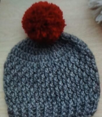 Handmade grey crochet baby pom pom beanie with textured pattern and red fluffy pom pom