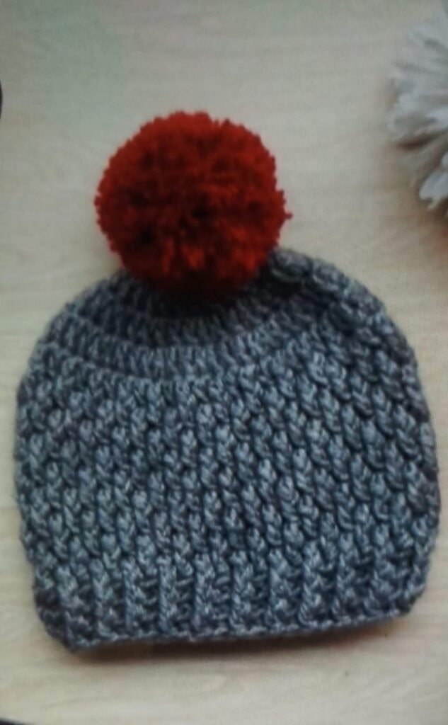 Handmade grey crochet baby pom pom beanie with textured pattern and red fluffy pom pom