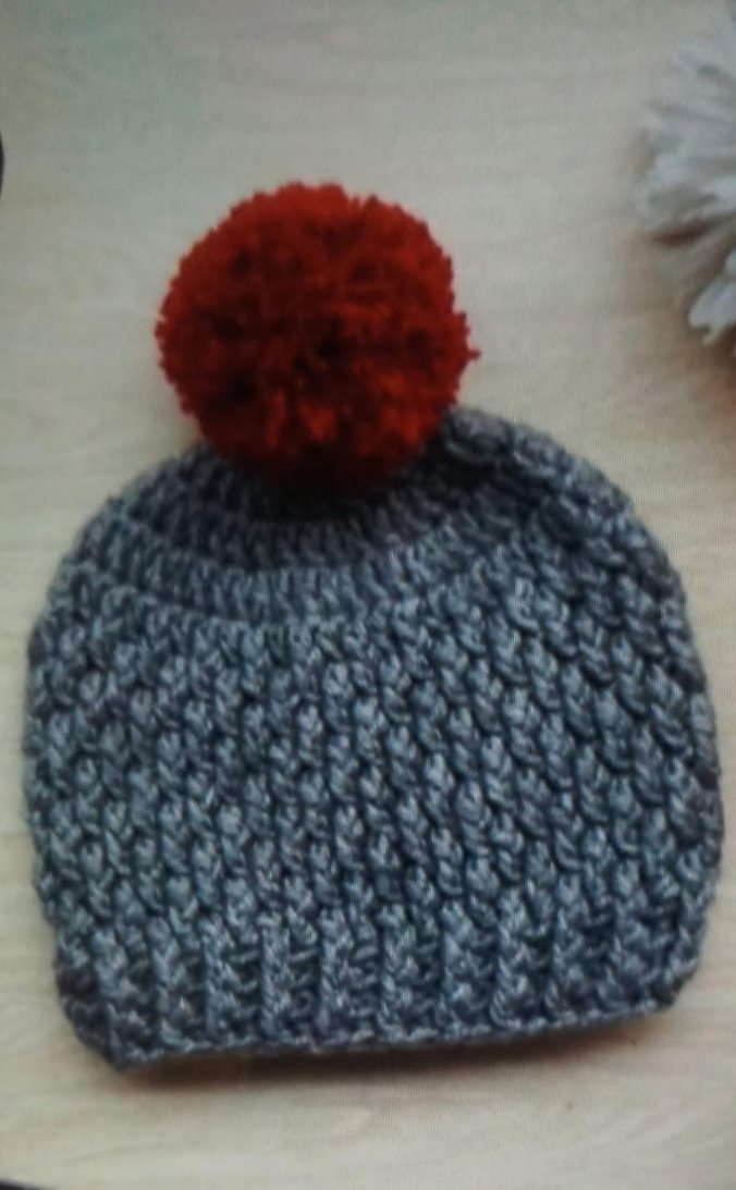 WhatsApp Image 2026-06-02 at 10.46.35 AM Handmade grey crochet baby pom pom beanie with textured pattern and red fluffy pom pom