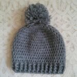 Handmade grey crochet pom pom beanie cap with textured pattern and ribbed edge