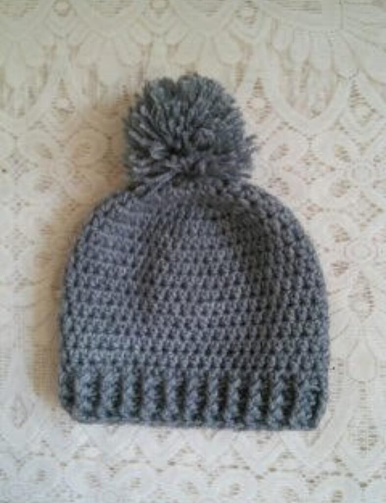 Handmade grey crochet pom pom beanie cap with textured pattern and ribbed edge