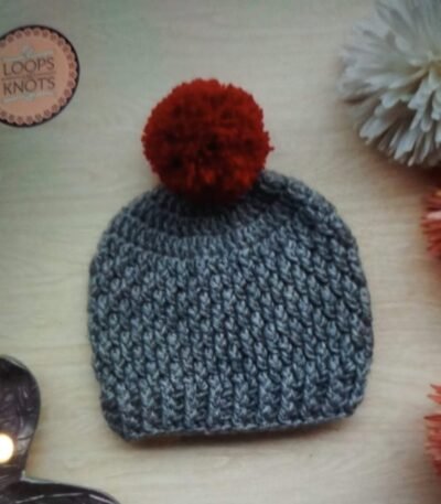 Handmade grey crochet pom pom baby beanie cap with textured pattern and red fluffy pom pom